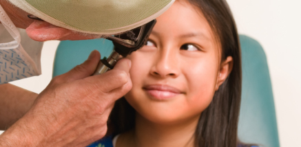 A medical professional using an ophthalmoscope to examine the eye of a smiling young girl.