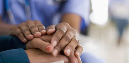 A close-up of two people holding hands in a gentle, comforting gesture.