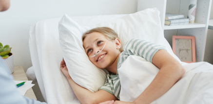 A young girl resting in a white hospital bed and smiling warmly.